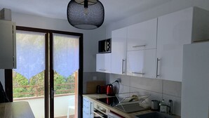 A compact kitchen with white cabinets, a built-in oven, a dishwasher, and a small countertop with a kettle and toaster. - The Isard appt (Vernet-les-Bains)