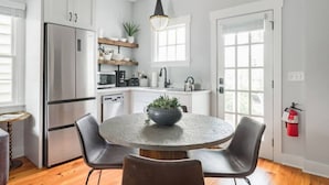 Une cuisine moderne avec des meubles blancs, un réfrigérateur en acier inoxydable, une table ronde avec des chaises et un luminaire suspendu.