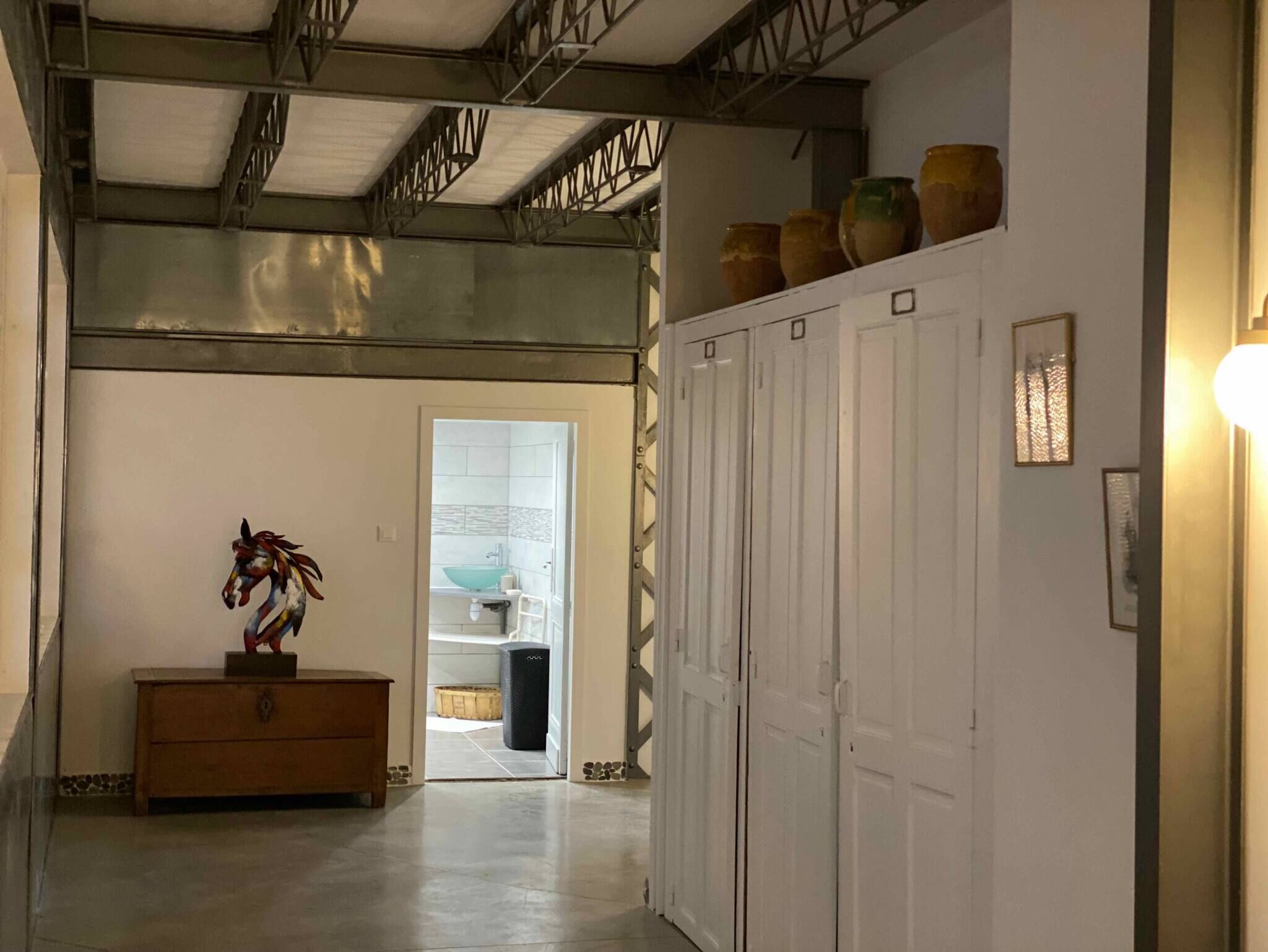 A hallway with a wooden bench, a horse sculpture, and a row of white doors.