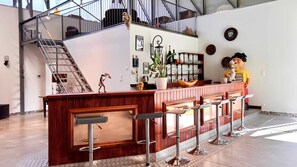 Eine Bar mit einer Holztresen, Metallhockern und einer Treppe im Hintergrund.