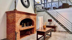 A brick fireplace with a clock above it, a staircase, and a table with a vase and candle.