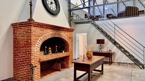 A brick fireplace with a clock above it, a staircase, and a table with a vase and candle.