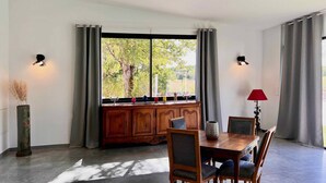 A dining area with a wooden table and chairs, a window with curtains, and a vase with dried plants.