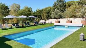 Ein rechteckiger Pool mit klar blauem Wasser, umgeben von einem gepflegten Rasen und mehreren Liegestühlen mit Sonnenschirmen.