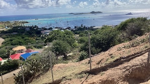 A coastal view with a clear sky, boats on the water, and a hilly landscape with buildings and greenery. - Greenheart Cottage (Clifton Union island)