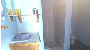 A bathroom with a wooden cabinet, a sink, and a shower enclosure. - Greenheart Cottage (Clifton Union island)