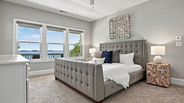 A bedroom with a large bed, two bedside lamps, a view of the outdoors, and a decorative wall piece. - Sleeps 22 on Lake Norman, Biggest Private Dock, Estate with Movie Theater, 2 Chef Kitchens, Game Room, Deep Water Lakefront, Covered Dock, Boat-Ready Year Round, Ideal for Family Reunions and Corporate Groups (Denver)
