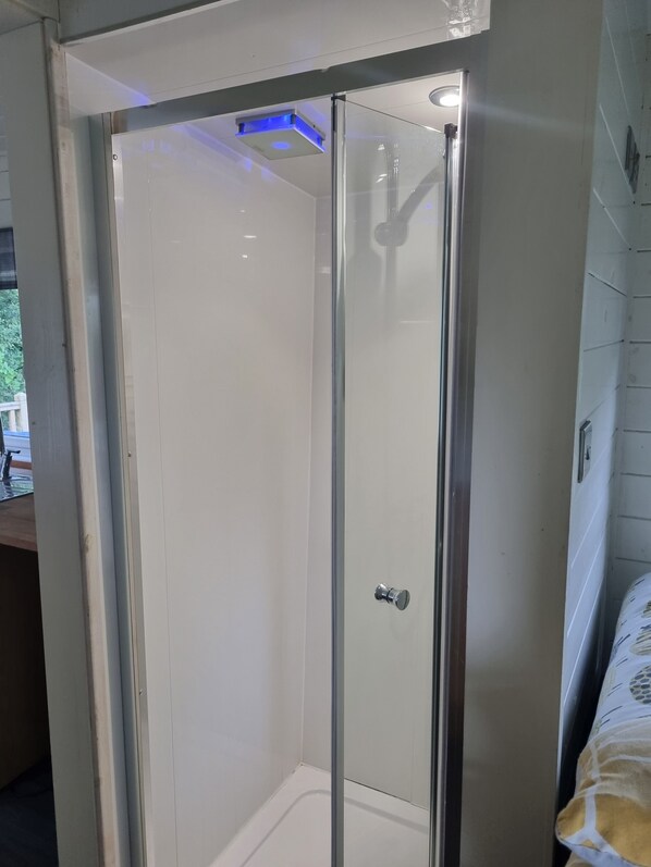 A glass-enclosed shower area with a white tiled floor and a visible showerhead.