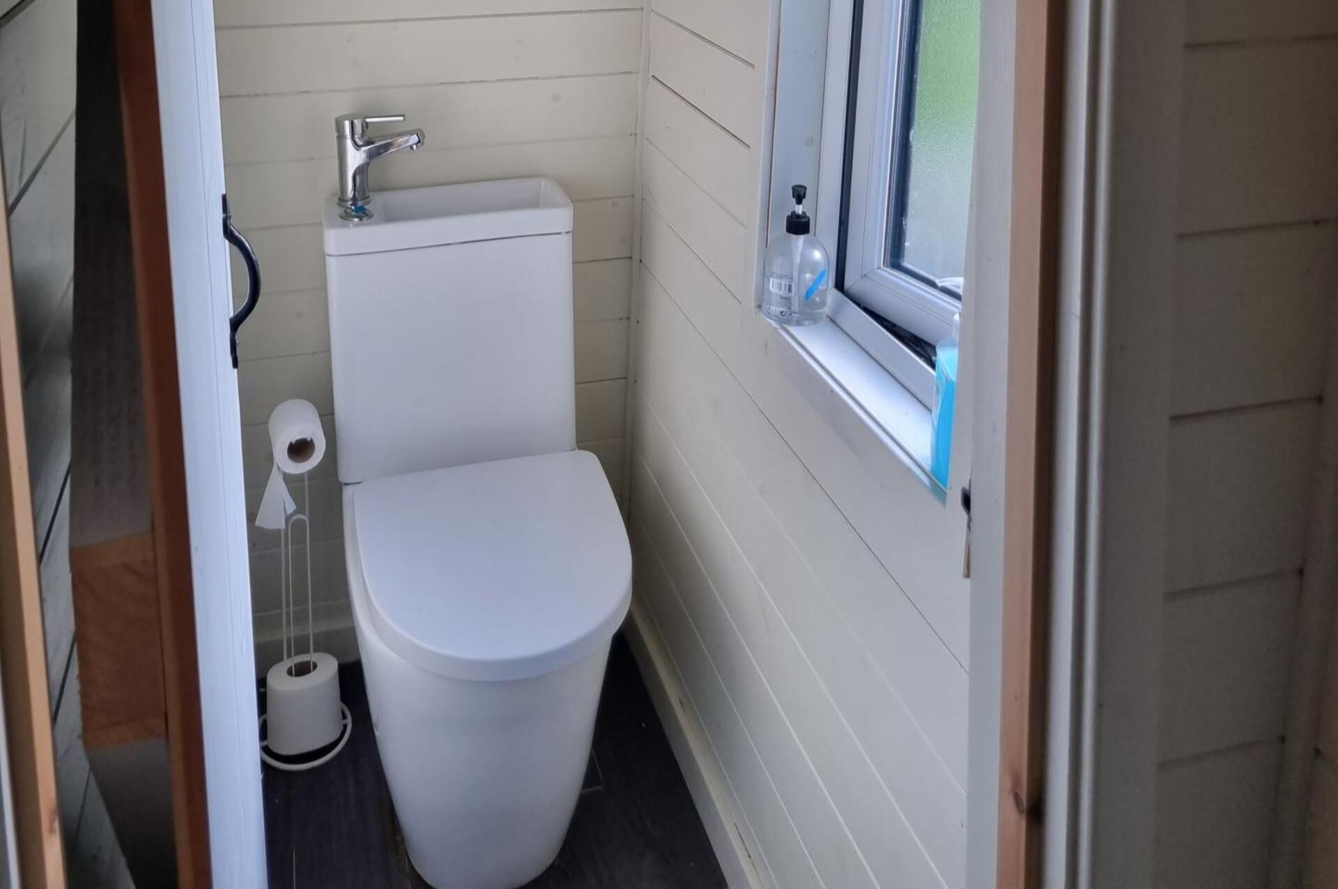 Pieni, käytännöllinen kylpyhuone, jossa on valkoinen wc-istuin, pesuallas ja ikkuna.