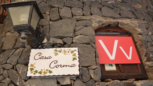 A stone wall with a lit lantern, a sign reading 'Casa Corma,' and a red sign with a white 'V' and a license plate.