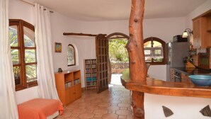 A cozy room with a bed, a wooden bookshelf, a kitchen area with a sink and stove, and a large window with curtains. - Casa Corma (Valle Gran Rey)