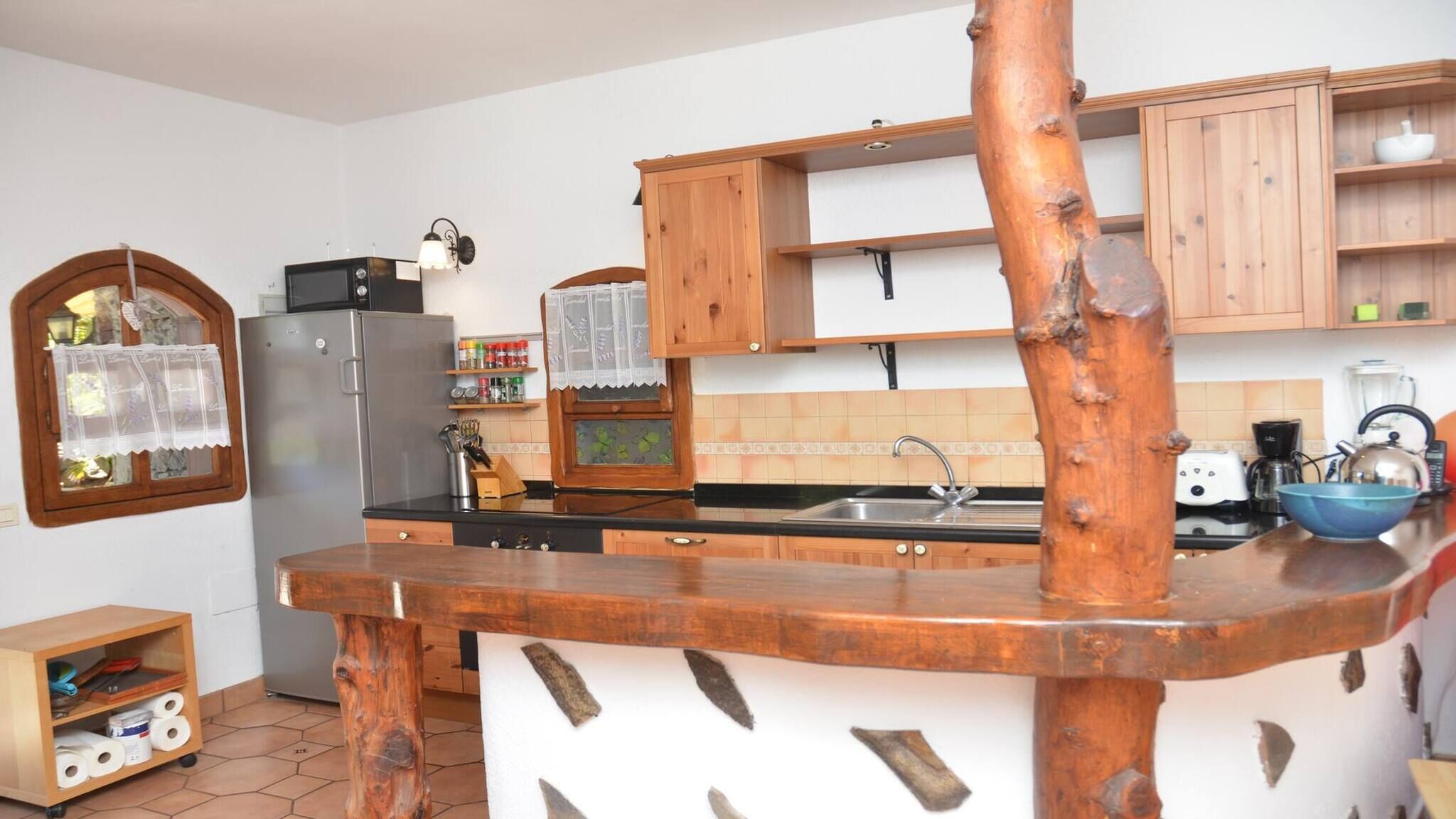 A kitchen with wooden cabinets, a stainless steel refrigerator, a sink, and a countertop with a blue bowl.