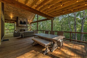 A wooden deck with a stone fireplace, wicker furniture, and a TV mounted on the wall.