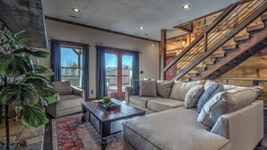A spacious living room with a large sectional sofa, a coffee table, and a staircase leading to an upper level.