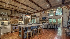 A spacious kitchen with a large island, wooden beams, stone accents, and a stone fireplace.