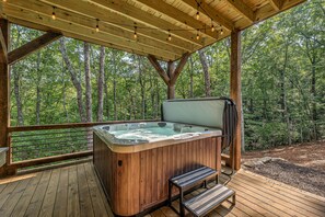 A wooden deck with a hot tub, benches, and a view of a forest.