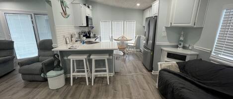 A compact kitchen with a central island, bar stools, a refrigerator, and a dining area with chairs.