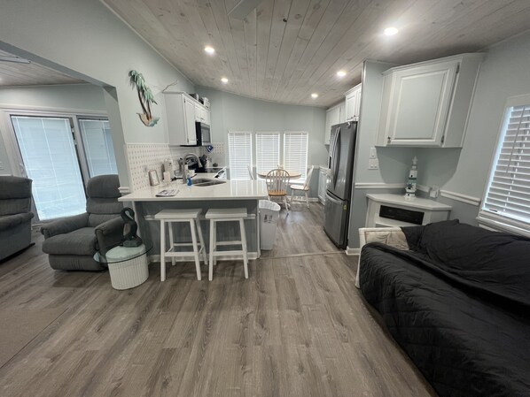 Una cocina compacta con una isla central, taburetes de bar, un refrigerador y un comedor con sillas.