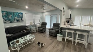Een ruime woonkamer met een bank, fauteuils, een glazen salontafel en een kleine hond.
