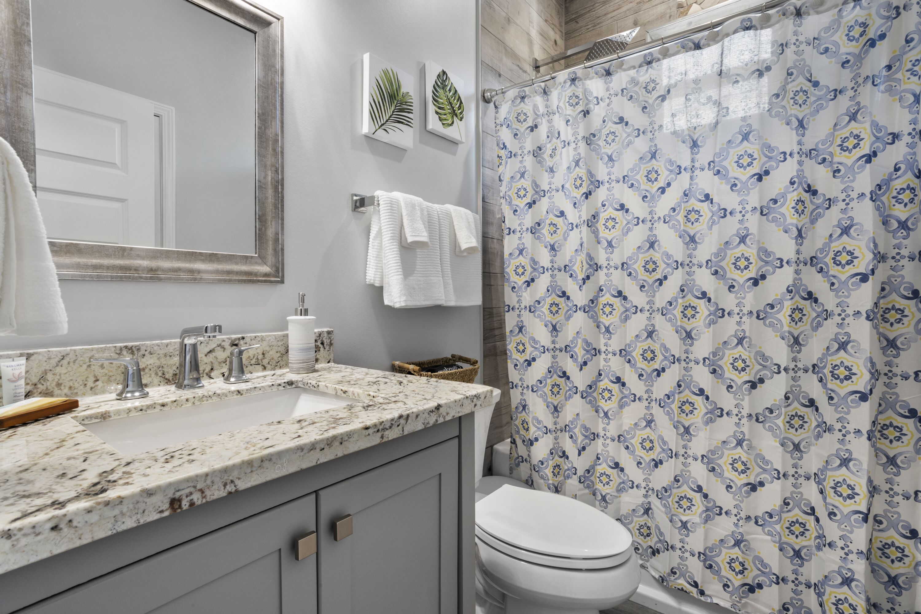 Un baño con lavabo de mármol, inodoro y cortina de ducha con diseño geométrico.