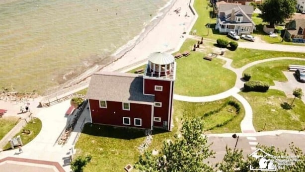 Vue aérienne d’une zone côtière, avec un bâtiment rouge imposant, une plage et des maisons résidentielles.