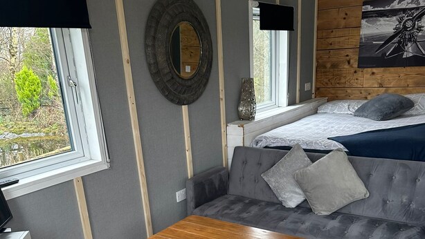 A cozy room with a grey sofa, a wooden coffee table, and a large mirror on the wall. - Glamping Hut - Sleeps up to 4 Hot Tub & Parking (Welshpool)
