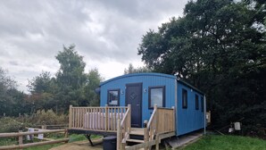 A small blue cabin with a wooden deck and a door. - Glamping Hut - Sleeps up to 4 Hot Tub & Parking (Welshpool)