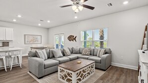 A spacious living room with a gray sectional sofa, a wooden coffee table, and a ceiling fan. - WaterView • NEW Boardwalk to Beach • Sleeps 15 • Resort Pools (Port St. Joe)