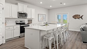 A modern kitchen with white cabinetry, a central island with bar stools, a microwave, and a stove. - WaterView • NEW Boardwalk to Beach • Sleeps 15 • Resort Pools (Port St. Joe)