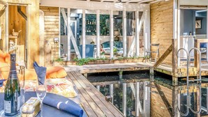 Un terrazzo in legno con un tavolo di vetro, una bottiglia di vino, un bicchiere e un piatto con una fetta di torta.