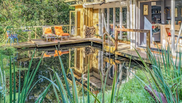 Una terrazza in legno con un ponte di vetro sopra l'acqua, circondata dal verde.