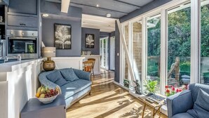 Una cucina moderna con forno integrato, un'area pranzo con tavolo e sedie bianche e ampie finestre che si affacciano sul verde.