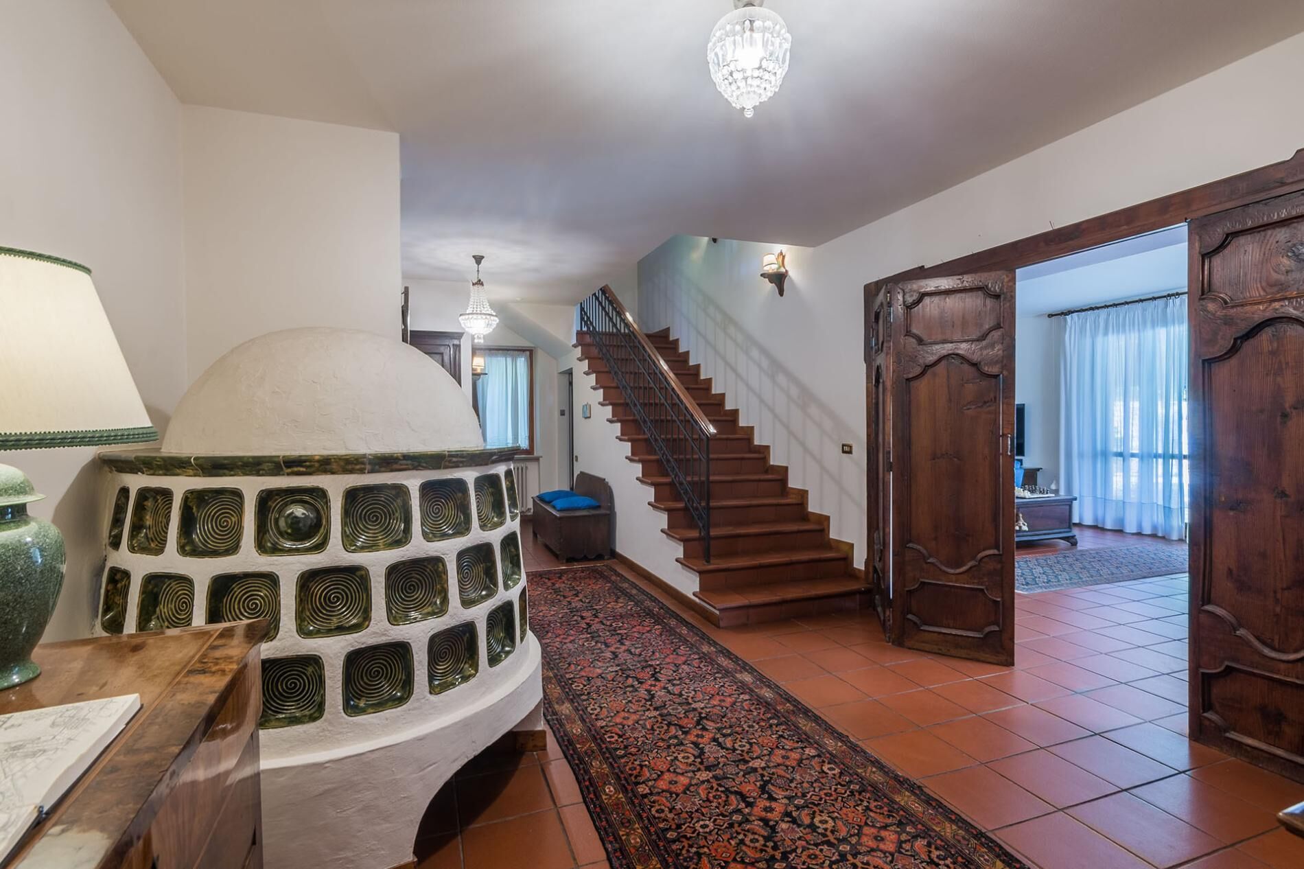 A spacious hallway with a grand staircase, a decorative wall, and a chandelier.