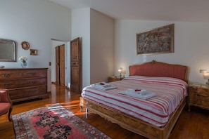 Quarto com cama de madeira, mesa de cabeceira, cômoda, cadeira e um quadro na parede.