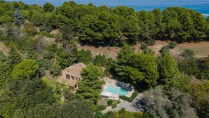 Vue aérienne d’une propriété dotée d’une piscine, entourée d’une forêt dense et offrant une vue dégagée sur la mer.