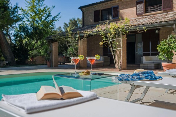 Uma área de piscina com dois copos de martini, um livro e uma espreguiçadeira.