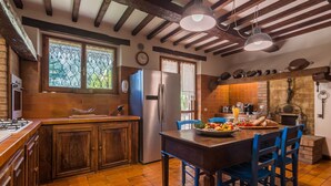 Une cuisine avec des meubles en bois, un îlot central doté de chaises bleues, un réfrigérateur et une fenêtre donnant sur un paysage verdoyant.