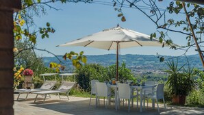 Une terrasse extérieure avec une table et des chaises, un grand parasol et une vue sur la campagne.