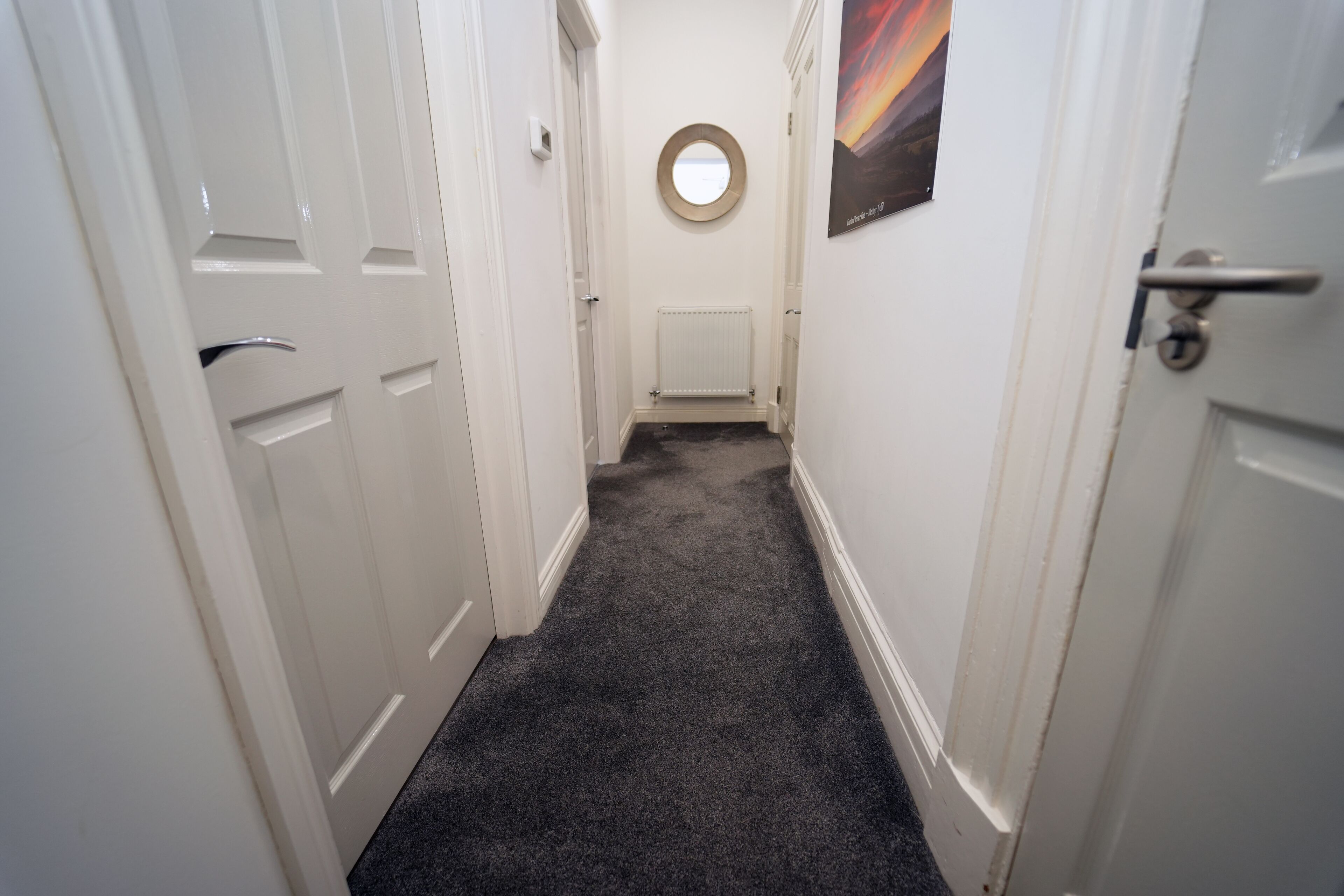 A narrow hallway with white doors, a carpeted floor, and a radiator.