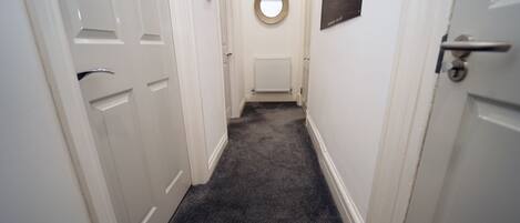 A narrow hallway with white doors, a carpeted floor, and a radiator.