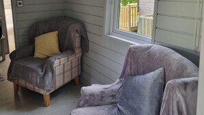 Habitación de esquina con un sillón a cuadros y un sofá acolchado, ambos cubiertos con mantas.