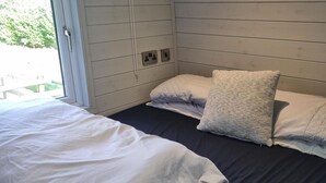 A bedroom with a bed, pillows, a window, and a wall socket. - Glamping Hut - Sleeps 2, hot tub & Parking (Welshpool)
