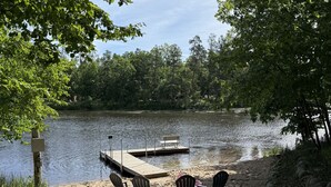 A lakeside setting with a dock, chairs, and a sandy beach.