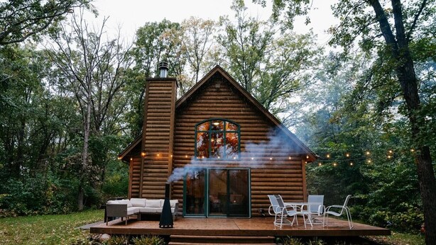 A log cabin with a chimney, a covered patio, and outdoor seating.