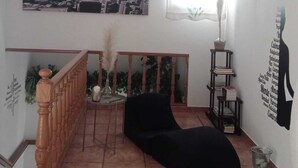 A living room with a black sofa, a cityscape painting, a window with a curtain, a staircase, and a bookshelf. - A Morada de Julia (Morgadans-Gondomar)