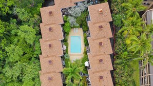 An aerial view of a resort with a central pool surrounded by multiple bungalow-style accommodations, each with a small deck and a view of the pool.