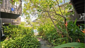 A narrow pathway flanked by dense foliage and a wooden structure with a sloped roof.