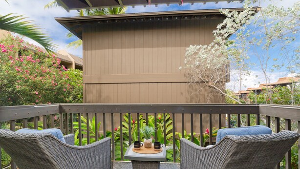 A balcony with wicker furniture, a table with two mugs, and a view of a building with a brown facade.