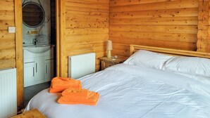 A wooden cabin room with a bed, a nightstand, a lamp, a sink, and a mirror. - 3 bedroom accommodation in Enochdhu, near Pitlochy (Enochdhu, near Pitlochy)