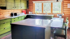 A kitchen with a central island, green cabinets, a sink, and a window with a view of trees. - 3 bedroom accommodation in Enochdhu, near Pitlochy (Enochdhu, near Pitlochy)